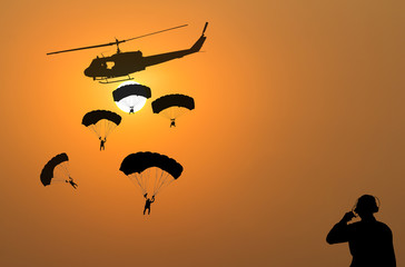 Fototapeta na wymiar Silhouette of parachute and helicopter on sunset background