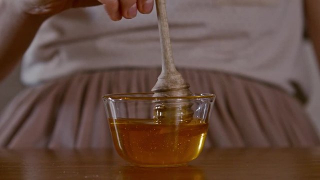 Hand on honey dipper from wooden cup