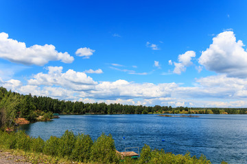 Obraz na płótnie Canvas Берег озера в солнечный день. Белые кучевые облака на фоне синего неба.