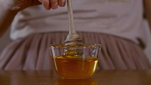 Hand on honey dipper from wooden cup