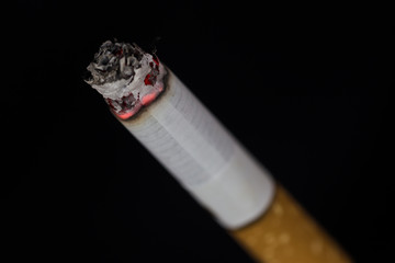 Burning cigarette with smoke on black background