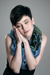 Cute pretty short hair woman pretending to sleep wearing colorful kerchief over gray studio background.