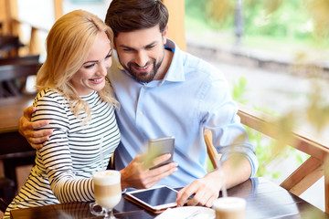 Cheerful lovers relaxing with technology in cafe