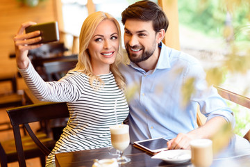 Joyful man and woman using smartphone in cafeteria