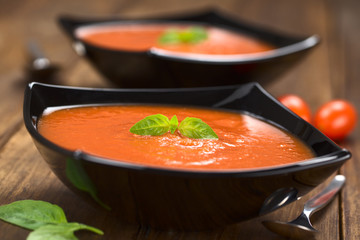 Frisch zubereitete Tomatensuppe mit Basilikumblatt in schwarzer Schale serviert (Selektiver Fokus, Fokus auf das Basilikumblatt auf der Suppe)