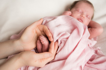 newborn baby feet in mother hands on pink fabric
