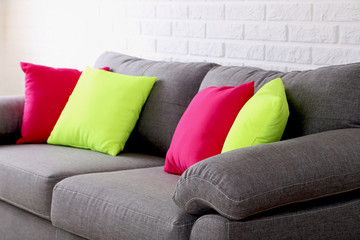 Colorful pillows on grey sofa on a brick wall background