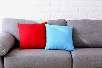 Colorful pillows on grey sofa on a brick wall background