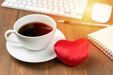 Coffee cup and hearth on wooden table with office gedgets in background. Sunlight filter effect