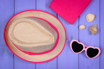Sunglasses, straw hat and towel on purple boards, accessories for summer