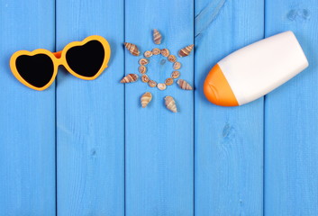 Seashells in shape of sun, sunglasses and sun lotion on blue boards, accessories for summer, copy space for text