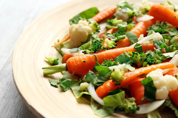 Fresh salad with baby carrots on wooden plate closeup