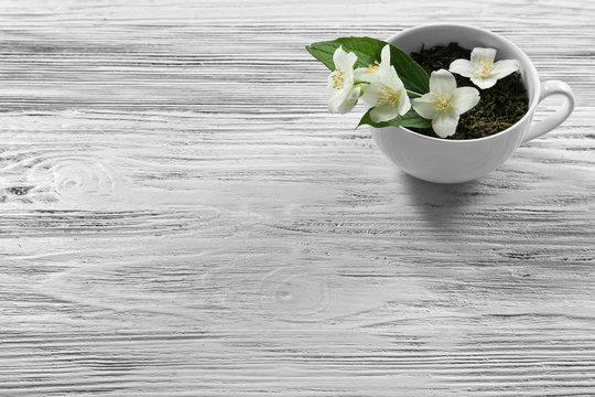 Cup of green tea leaves and jasmine flowers on wooden background