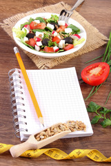 Fresh greek salad with vegetables, centimeter and notepad for writing notes, healthy nutrition and slimming concept