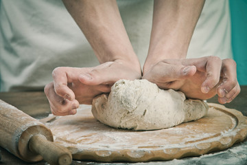 Fototapeta premium Making dough by mens hands on wooden table background