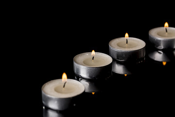 Fototapeta na wymiar Lit Tea Candles with Reflection on Black