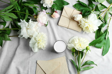 Composition with beautiful peony flowers and envelopes on white fabric, top view