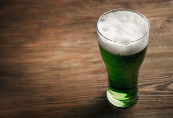 Glass of green beer on wooden background