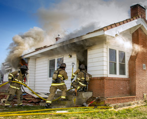 Fire fighters in full breathing apparatus enter a smoke filled house on fire.