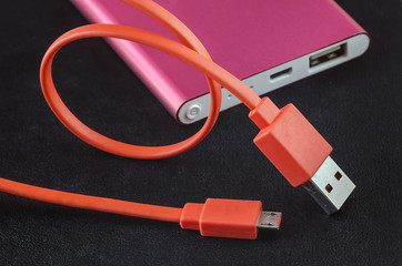 Orange color USB cable and red power bank on black leather backg