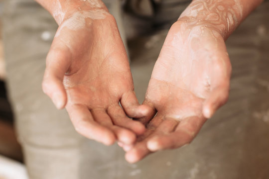 Potter messy palms in clay, working hands of craftsman. Closeup