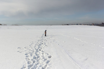 The little boy in a color jacket walking on the snow riverbank