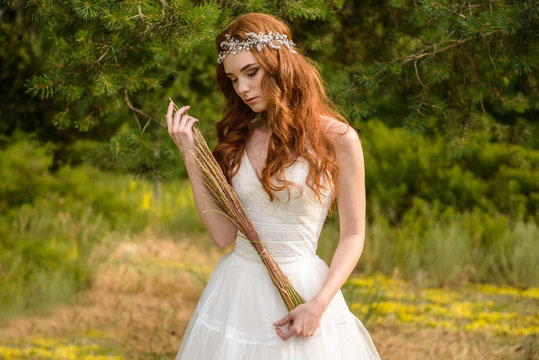 Redheaded young girl in the woods. Portrait of the bride in the Park. A girl holds wheat ears in the hands.