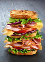 Big sandwich with ham and vegetables on dark wood background