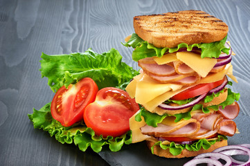 Big sandwich with ham and vegetables on dark wood background
