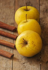 fresh autumn yellow apples on wooden table with cinnamon sticks