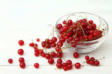Red currants in bowl on white wooden background