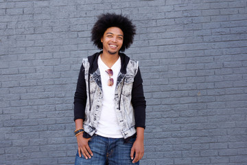 Young man with afro smiling standing in front of gray wall