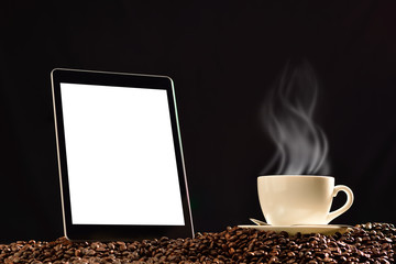 Tablet computer with blank white screen and cup of coffee with smoke on pile of coffee beans