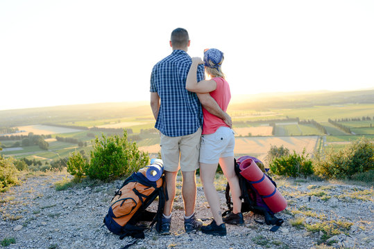 young couple with backpack on adventure mountain trek admiring a beautiful sunset landscape