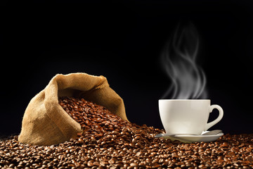 Cup of coffee with smoke and coffee beans in burlap sack on black background