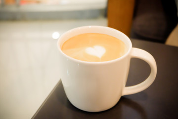 A cup of heart shape latte coffee under warm light 