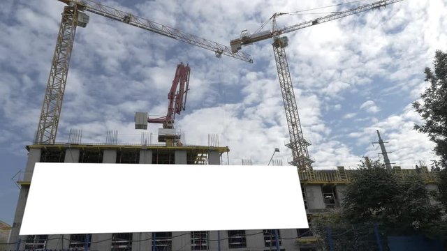 Low angle shot of a building under construction with blank banner and cranes against blue cloudy sky background. Construction industry