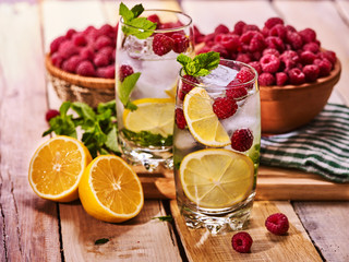 On wooden boards is cocktail glass with berries lemon and ice cubes. Alcohol country cocktail number eighty five with berry basket mint and ice cubes. Country life cocktail.