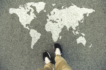 World map on an asphalt road. Top view of the legs and shoes. POV - obrazy, fototapety, plakaty