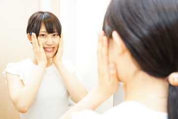 Obraz na płótnie Canvas 鏡の前でスキンケアをする若い日本人の女性 美容 化粧 ミラー 一人暮らし 美人 美肌