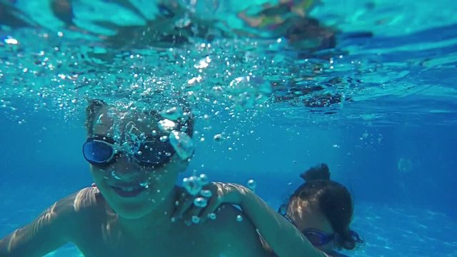 Young Cute teen boy dives in blue pool and wearing goggles at camera.