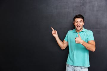 Happy young man pointing away and showing thumbs up