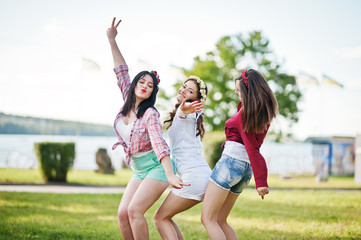 Three happy girls in short shorts and wreaths on heads dancing a