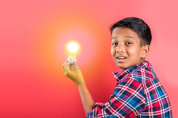 10 year indian boy holding glowing light bulb in hand, creativity concept, science concept, idea clicking expressions, indian boy, asian boy, red background, front profile, closeup