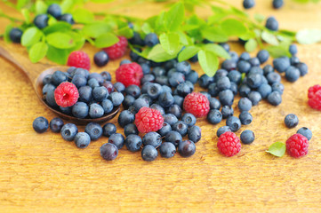 Juicy mature berries of bilberry and raspberry in in a wooden spoon on a wooden surface.