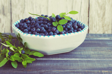 Berries of ripe juicy bilberry in a plate on a wooden table.