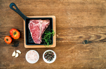 Raw uncooked meat t-bone steak with garlic, tomatoes, rosemary, salt and pepper in small dark...