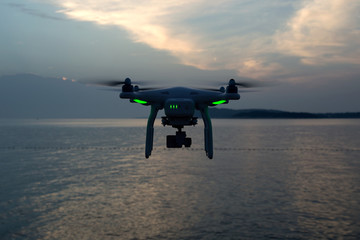 Professional drone with green lights flying over sea in the dark