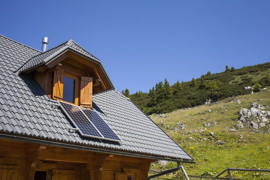 Mountain cottage with solar panels, against clear blue sky, space for text