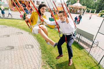 Emotional newlyweds laughing while riding on high carousel in amusement park. Expressive wedding couple at carnival.